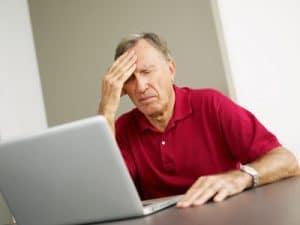 Senior man using laptop computer with headache and eyes closed