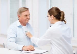 Female doctor listening to heart beat of elderly man
