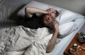 Man with headache trying to fall asleep in bed with medication on nightstand